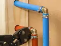 Instalacja hydrauliczna z rurami pex. Narzędzie do zaciskania łączy pomarańczową rurę z mosiężnym kolankiem.