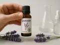 Mano sostiene botella de aceite esencial de lavanda, rodeada de flores. Descubre sus propiedades relajantes.