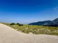 Sentiero ghiaioso verso la cima Blockhaus, con prati verdi e montagne sullo sfondo sotto un cielo azzurro.