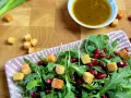 Frischer Rucola Salat mit Granatapfelkernen und Croutons, dazu ein Dressing.