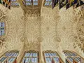 Intricate fan vaulting of a grand hall, reminiscent of the detailed ceilings found in abbey graves, adorned with flags.