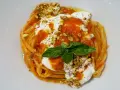 Un piatto invitante di pasta con stracciatella, salsa di pomodoro, pistacchi tritati e una foglia di basilico fresco.