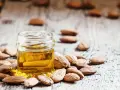 Aceite de almendras para que sirve: un frasco de aceite dorado rodeado de almendras sobre madera rústica.