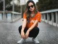 Mujer con estilo smart casual, con camiseta naranja a rayas, pantalones negros y zapatillas deportivas.