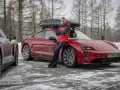 Mężczyzna w czerwonej kurtce opiera się o czerwonego Porsche Taycan z boxem dachowym.