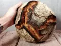 Hand hält ein knuspriges Sauerteigbrot. Die Kruste ist dunkelbraun und rissig. Was ist Brotmehl? Es ist die Grundlage für dieses köstliche Gebäck.