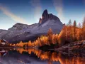 Riflessi dorati sull'acqua di un lago alpino, con un rifugio e montagne innevate. Perfetto per le camminate a Cortina d'Ampezzo.