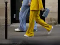 Un outfit tailleur con sneakers, giallo brillante e azzurro polvere, camminano sul marciapiede.