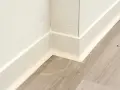 Angolo di una stanza con parquet grigio e battiscopa bianco appena installato.