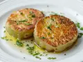 Dos rodajas de patatas al caliu doradas y tiernas, bañadas en aceite de oliva y espolvoreadas con perejil fresco.