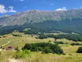 Vasta distesa verde ai piedi del monte Mileto, con un edificio circolare rosso e una strada tortuosa.