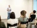 Mężczyzna z tabletem przemawia do grupy słuchaczy. Widać, że jego **charyzma co to** jest widoczna w sposobie, w jaki angażuje publiczność.