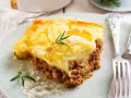 Zapiekanka pasterska (Shepherd's Pie) z warstwą mielonego mięsa i ziemniaków, ozdobiona rozmarynem.