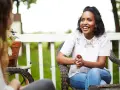 Two women are sitting on a porch, one animatedly sharing the gospel with the other.