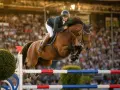 Cavalier et cheval brun en plein saut d'obstacles lors d'un parcours cso devant une foule en délire.