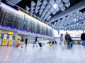 Tablica odlotów na lotnisku, ludzie z bagażami spieszą na boarding.