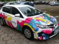 Kolorowe oklejone samochody z logo "Koutigo" na parkingu.