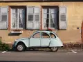Jasnoniebieski, zabytkowy Citroen 2CV, jeden z klasycznych modele stare, parkuje przed kamiennym domem z drewnianymi okiennicami.