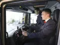 Dwóch młodych mężczyzn w garniturach ćwiczy jazdę ciężarówką na symulatorze. Zastanawiają się, ile zarabia kierowca na godzinę.