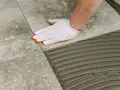 Ręka w białej rękawiczce układa płytkę gresową na kleju. Różnica między gres a płytkami jest widoczna w procesie układania.