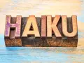 Träbokstäver bildar ordet "HAIKU" på en sliten träyta. En hyllning till den korta, poetiska formen.