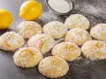 Deliziosi biscotti al limone spolverati di zucchero a velo, con limoni freschi sullo sfondo.