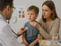 Lekarz bada chłopca, martwiąca się matka obok. Na ścianie wiszą plakaty o objawach odwodnienia, co może być związane z jelitówką u dzieci.
