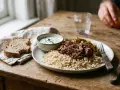 Assiette de riz brun, effiloché de bœuf et légumes, avec une sauce blanche et du pain. Une alimentation équilibrée pour la musculation.