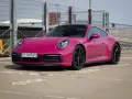 Różowy Porsche 911 Carrera 4S z czarnymi felgami i naklejką PORSCHE na progu, zaparkowany na zewnątrz.