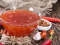 Schüssel mit leuchtend roter Sweet Chili Sauce, umgeben von frischen Chilis, Knoblauch und Gewürzen. Perfekt für ein Sweet Chili Sauce Rezept!