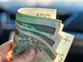 Dłoń trzyma zwitek polskich banknotów 100 zł. Dokument orzeczenie o niepełnosprawności może pomóc w uzyskaniu zasiłek pielęgnacyjny.