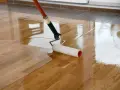 Application d'une couche de vitrificateur sur un parquet en bois. Le temps de séchage entre 2 couches est crucial pour un résultat parfait.