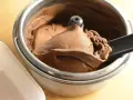 Un cucchiaio nero preleva una porzione di cremoso gelato fatto in casa al cioccolato da una gelatiera.