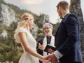Piękna panna młoda i pan młody słuchają celebransa, który wygłasza cytaty na błogosławieństwo pary młodej podczas ceremonii na łonie natury.