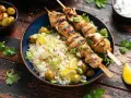 Deliciosos pinchitos de pollo a la parrilla servidos con arroz blanco, aceitunas verdes, rodajas de limón y cebolleta picada.