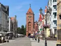 Ulica w Elblągu, z charakterystyczną wieżą i kolorowymi kamienicami. To najniżej położone miasto w Polsce, pełne urokliwych zakątków.