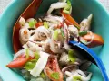 Ensalada tailandesa con fideos de cristal, calamares, tomate y cebolla, servida en un cuenco azul. El plato de sepia en salsa se ve fresco y apetitoso.
