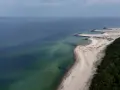 Plaża w Jarosławcu, zwana czasem "plażą dubaj", z kamiennymi falochronami i zielonym lasem.