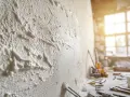 Gros plan sur un tableau avec enduit texturé, des outils de chantier et une fenêtre ensoleillée en arrière-plan.