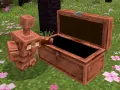 Un golem de cobre, con su cuerpo brillante, se asoma a un cofre abierto en un campo cubierto de flores rosadas.