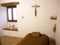 A monk's simple cell, showing where monks sleep: a narrow bed with a wooden block for a pillow, a crucifix, and a window.