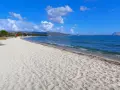 Spiaggia Cala d'Ambra: sabbia dorata, mare azzurro e montagne all'orizzonte. Un angolo di paradiso per rilassarsi.