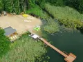 Plaża i pomost nad jeziorem, idealne miejsce na wypoczynek na Pojezierzu Brodnickim. Widać łódki, leżaki i budynek zadaszony.