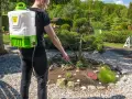 Domowy sposób na chwasty: mężczyzna z plecakowym opryskiwaczem pielęgnuje rabatkę, dbając o piękny ogród.