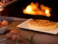 Une omelette mere poulard dorée et moelleuse, prête à être dégustée près d'un feu de cheminée. Des œufs frais sont visibles à côté.