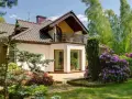 Dom z balkonem i tarasem, otoczony bujną zielenią i kwitnącymi rododendronami. Występ ściany podkreśla nowoczesny charakter budynku.