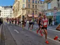 Corredores compiten en una media maratón en Europa, con edificios históricos y público animando.