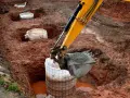 Koparka zasypuje betonem fundament palowy w wykopie. W tle widać kolejne przygotowane do zalania pale.