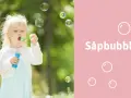 Liten flicka blåser stora såpbubblor i en grönskande trädgård. Kanske hon följer ett recept för extra stora bubblor!