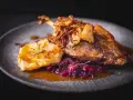 Pieczona kaczka z chrupiącą cebulką, purée i czerwoną kapustą na talerzu.